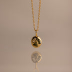 Mixed Peridot Capsule Pendant Necklace with a round pendant featuring geometric shapes, reflected on a smooth surface.