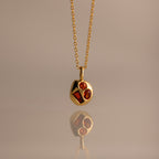 Mixed Garnet Capsule Pendant Necklace with a round pendant featuring three red gemstones, reflected on a smooth surface.