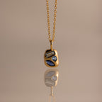 Mixed Blue Zircon Capsule Pendant Necklace, featuring three uniquely shaped blue zircons in a capsule pendant, reflected on a smooth surface.