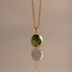 Mixed Emerald Capsule Pendant Necklace featuring green gemstones in a capsule-shaped pendant, elegantly reflected on a smooth surface.