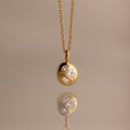 The Mixed Diamond Capsule Pendant Necklace features a gold capsule design with a round pendant set with clear gemstones, displayed on a neutral background.
