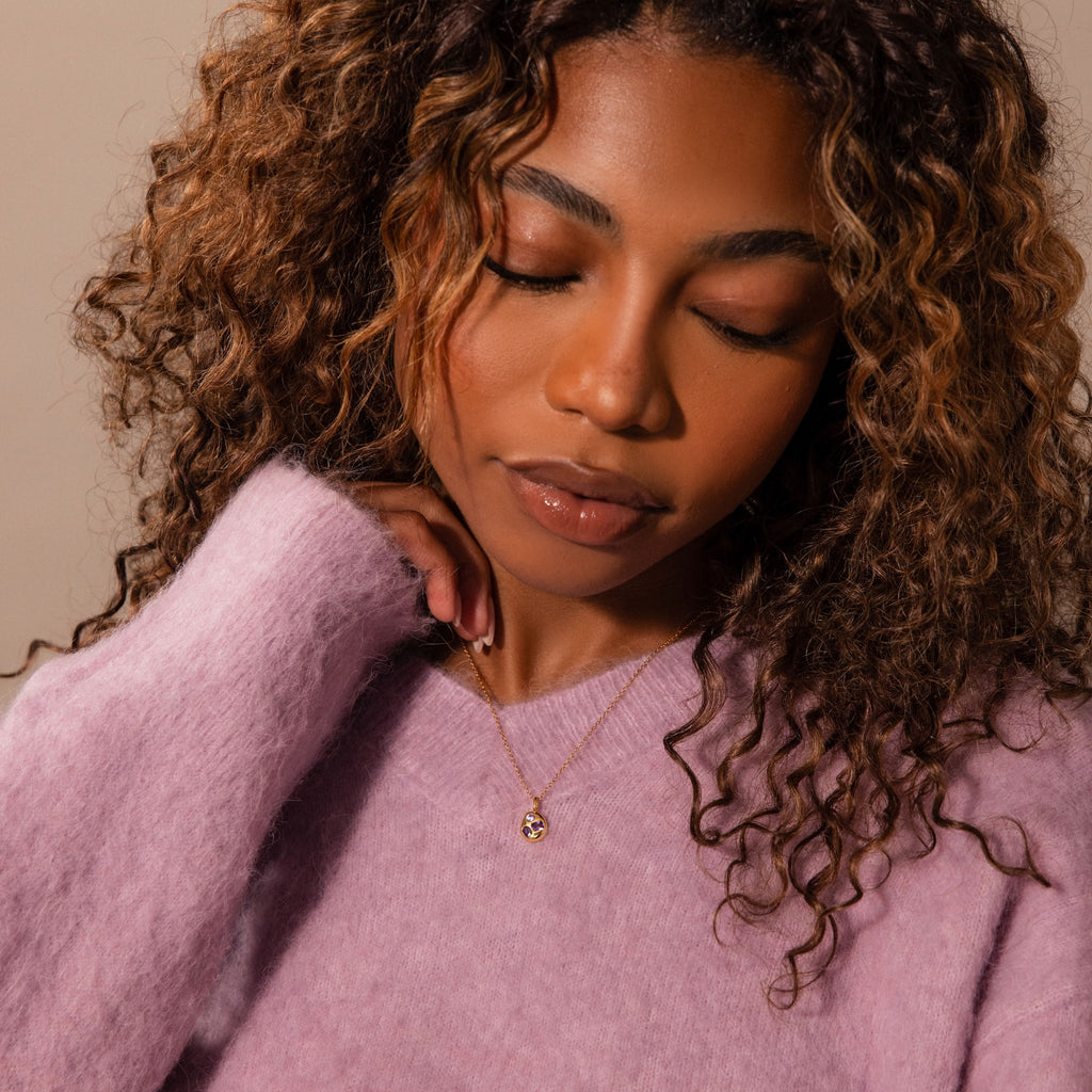 Woman with curly hair in a lavender sweater, eyes closed and touching her chin, wears the Mixed Aquamarine Capsule Pendant Necklace.