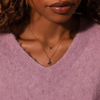 A woman wears the Mixed Peridot Capsule Pendant Necklace with a gold necklace and a soft lavender V-neck sweater.
