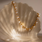 The Pearl & Diamond Tennis Bracelet is draped elegantly over a pearly white seashell, showcasing its luxurious blend of gold, pearls, and diamonds.