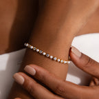 A close-up of the Pearl & Diamond Tennis Bracelet, adorned with pearls and diamonds, elegantly displayed on a wrist with gently touching hands.