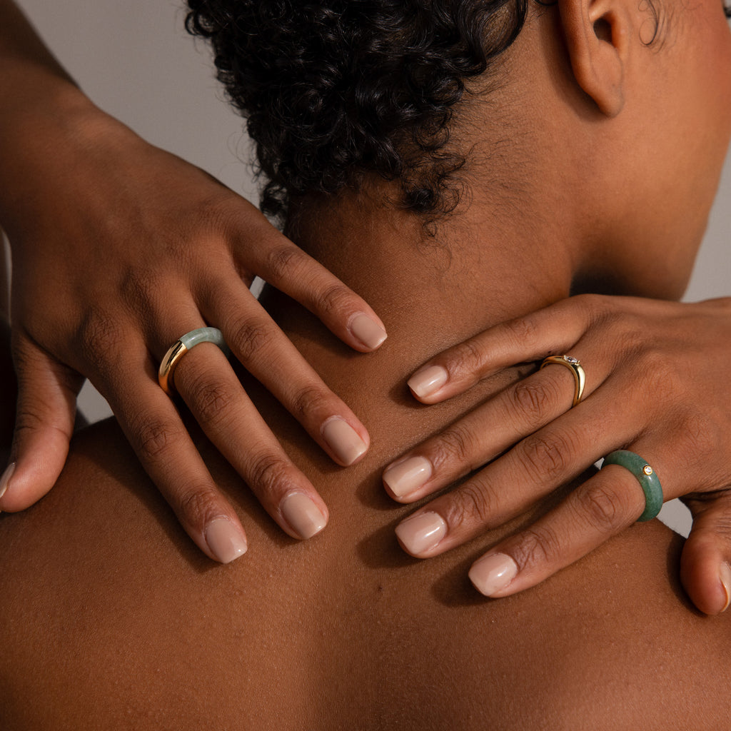 A person with short curly hair rests hands on bare shoulders, highlighting statement jewelry featuring the Half Jade Ring on their finger.