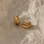 The Duo Pave Dome Studs—one plain, one with pavé diamonds—sit on crumpled beige paper, offering a perfect pair of everyday earrings inspired by classic curves.