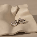 The Duo Pave Dome Studs in White Gold, adorned with small diamonds, rest on a wavy cream ceramic dish—an ideal choice for everyday elegance.