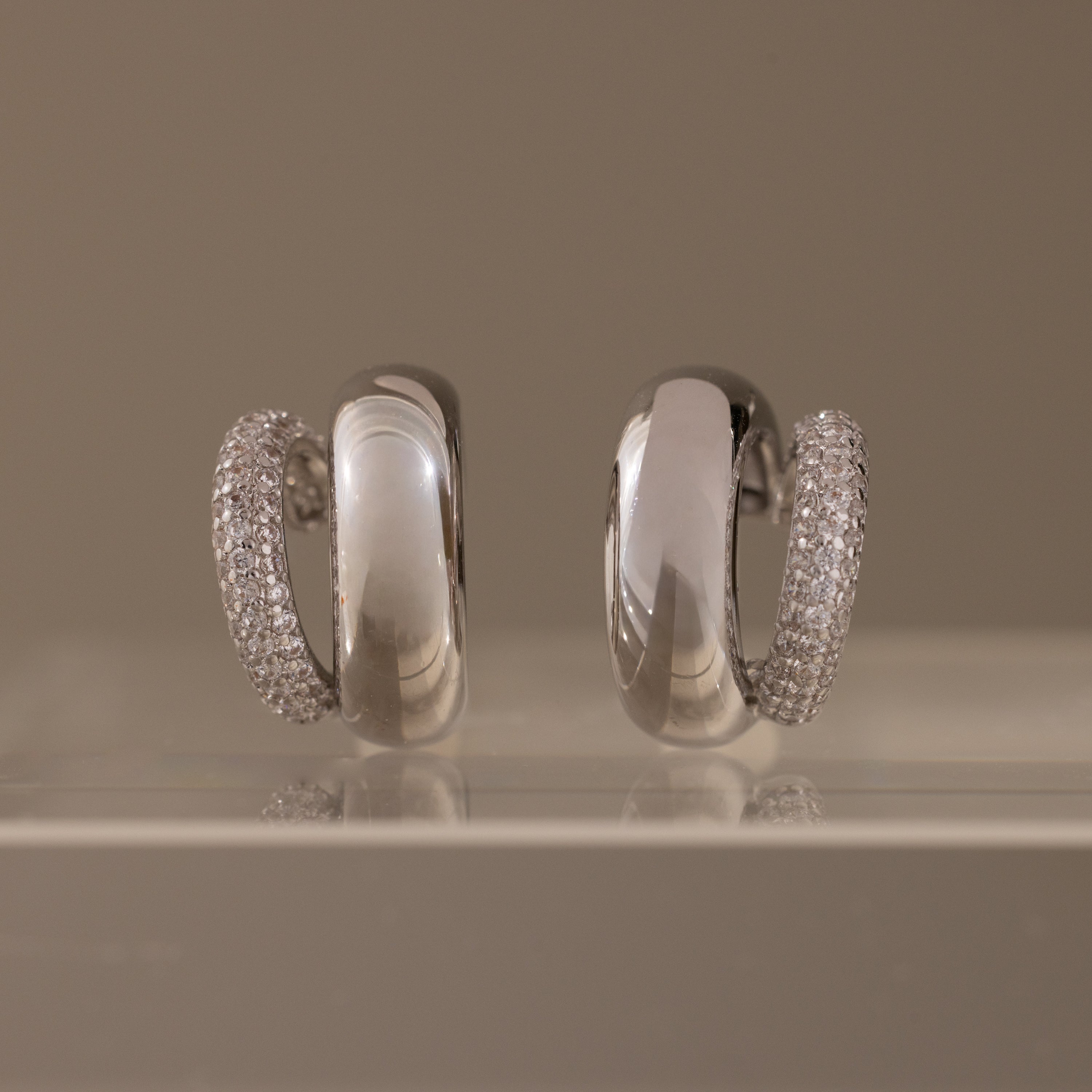 Duo Pave Dome Studs in White Gold, featuring one earring encrusted with clear pavé stones, are displayed on a clear surface—perfect as standout everyday jewelry.
