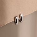 Bold Link Hoops in White Gold rest on a textured beige surface under soft lighting, highlighting the modern elegance of this jewelry piece.