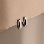 Bold Link Hoops in White Gold rest on a textured beige surface under soft lighting, highlighting the modern elegance of this jewelry piece.