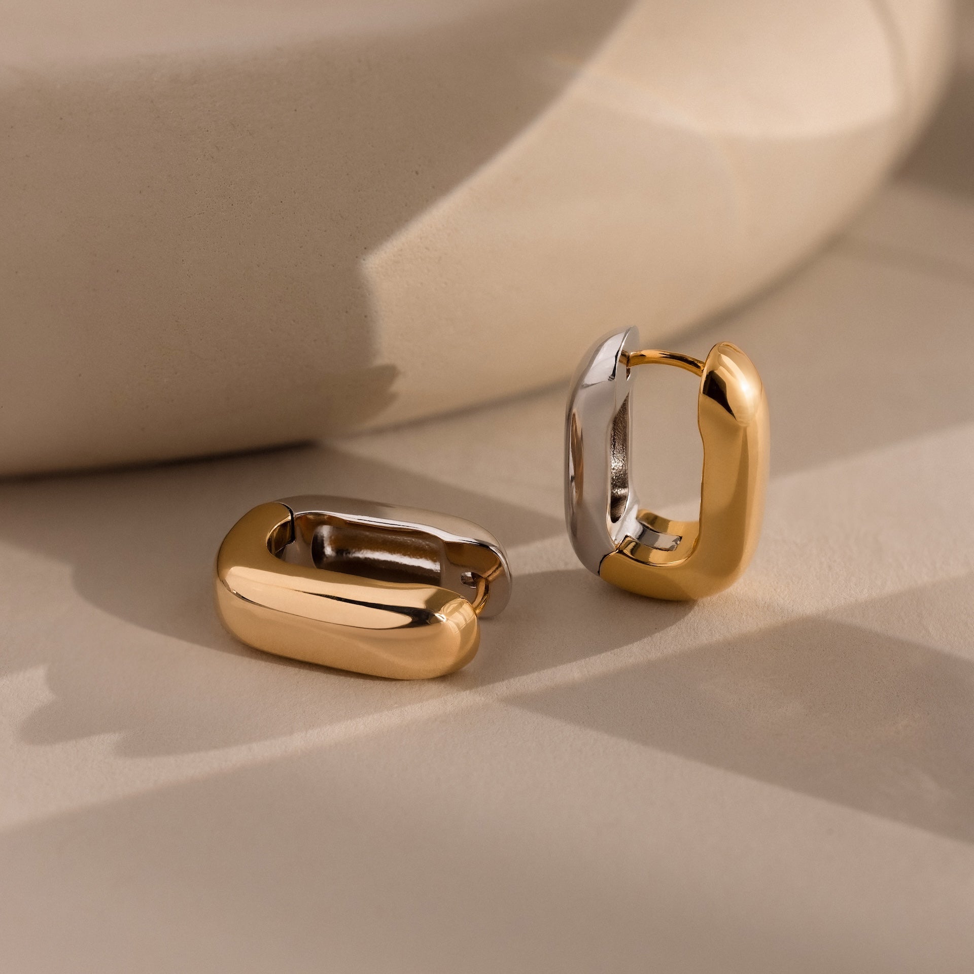 The Bold Link Hoops in Mixed Metal—one gold, one silver—rest on a neutral surface, highlighting their sculptural style and modern earring design.