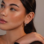 A woman with smooth skin wears Bold Link Hoops, gazing to the side with her hand resting on her shoulder.