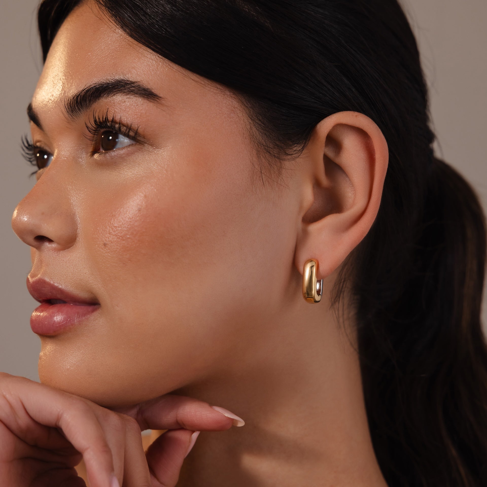 A woman with smooth skin wears Bold Link Hoops in Mixed Metal, gazing left with her hand on her chin and hair tied back.
