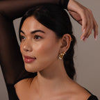 Woman with long dark hair wears the Laced Mixed Metal Huggies and a sheer black top, posing with her hand raised above her head.