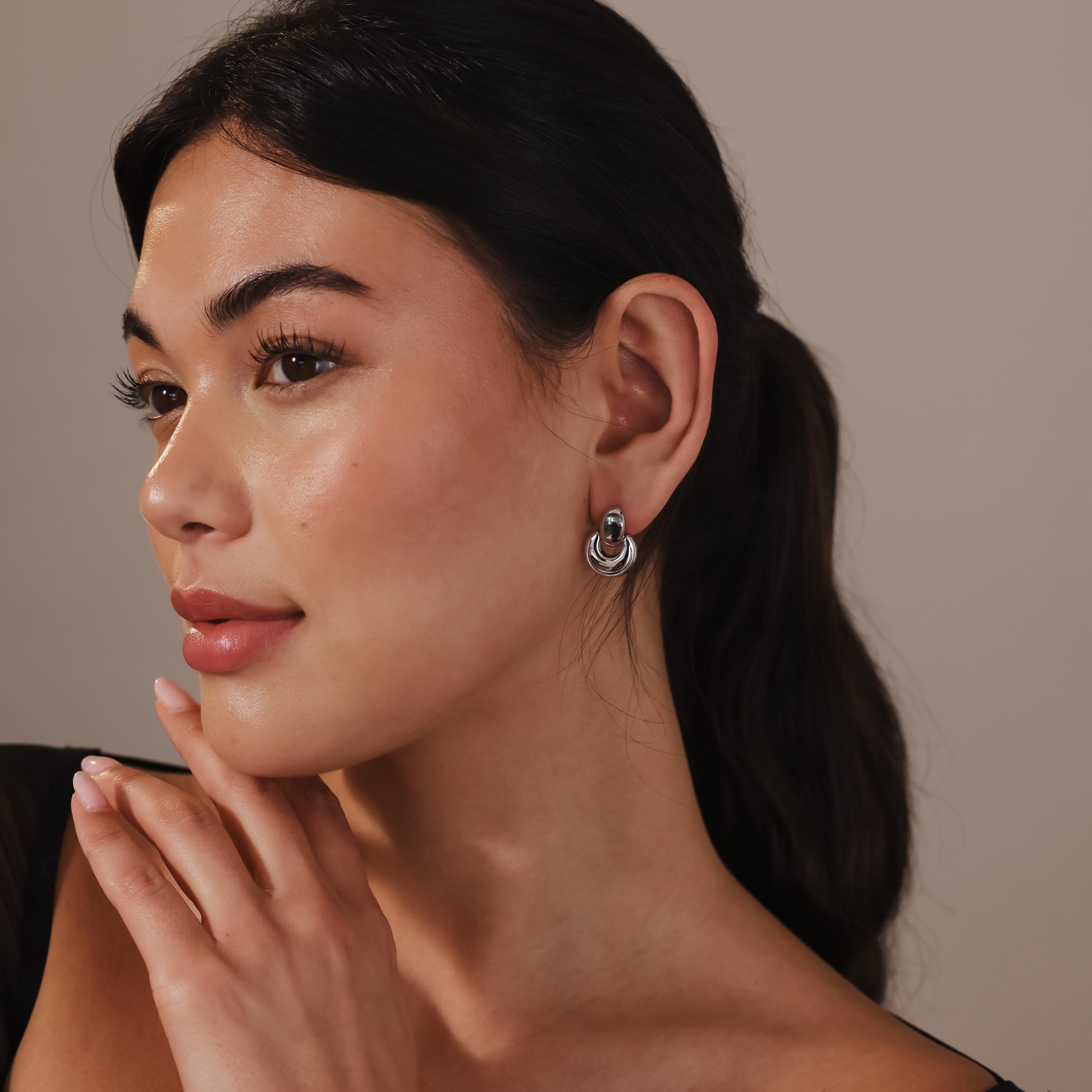 Woman with long dark hair in a ponytail wears Eclipse Dome Studs in White Gold, touching her chin and gazing to the side.