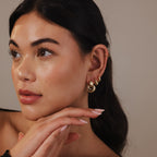 Woman with smooth skin and sculptural Eclipse Dome Studs, gazing left with hands gently posed under her chin, highlighting the elegance of modern jewelry.