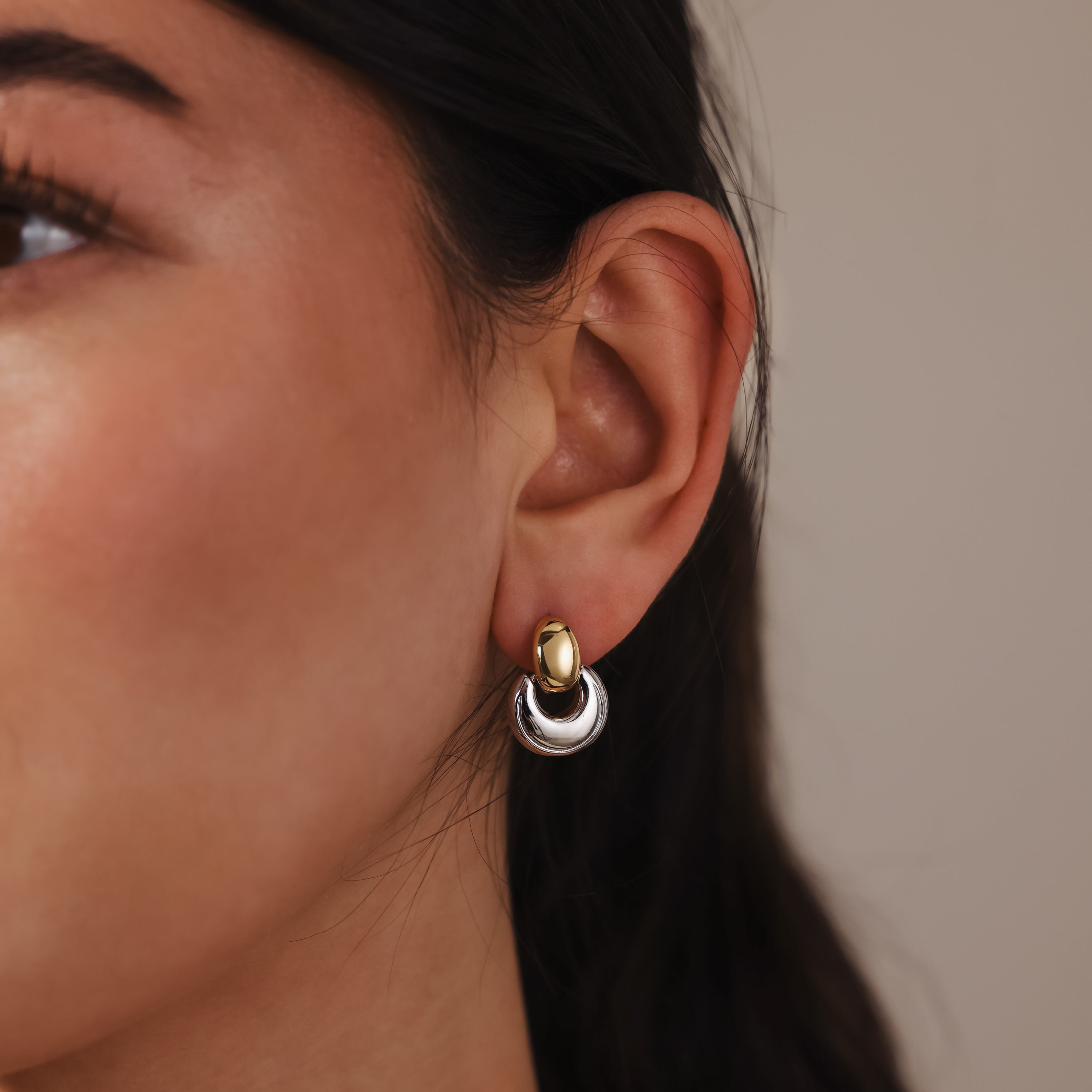 A close-up of a woman's ear adorned with Eclipse Dome Studs, featuring sculptural two-tone gold and silver hoops that highlight a modern jewelry style.