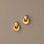 The Eclipse Dome Studs in 18K Gold are semi-circular, shiny dome earrings shown on a plain taupe background—perfect for fans of modern jewelry.