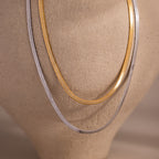 Two herringbone chain necklaces, one gold and one silver, draped over a mannequin bust.