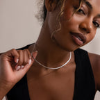 Woman adjusting a silver herringbone necklace against a neutral background