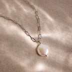 Silver link chain pearl pendant necklace on a beige sandy textured surface