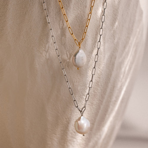 Two link chain pearl necklaces in gold and silver on a beige stone background