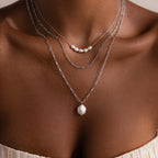 Close-up of a person wearing multiple silver necklaces on a neutral background