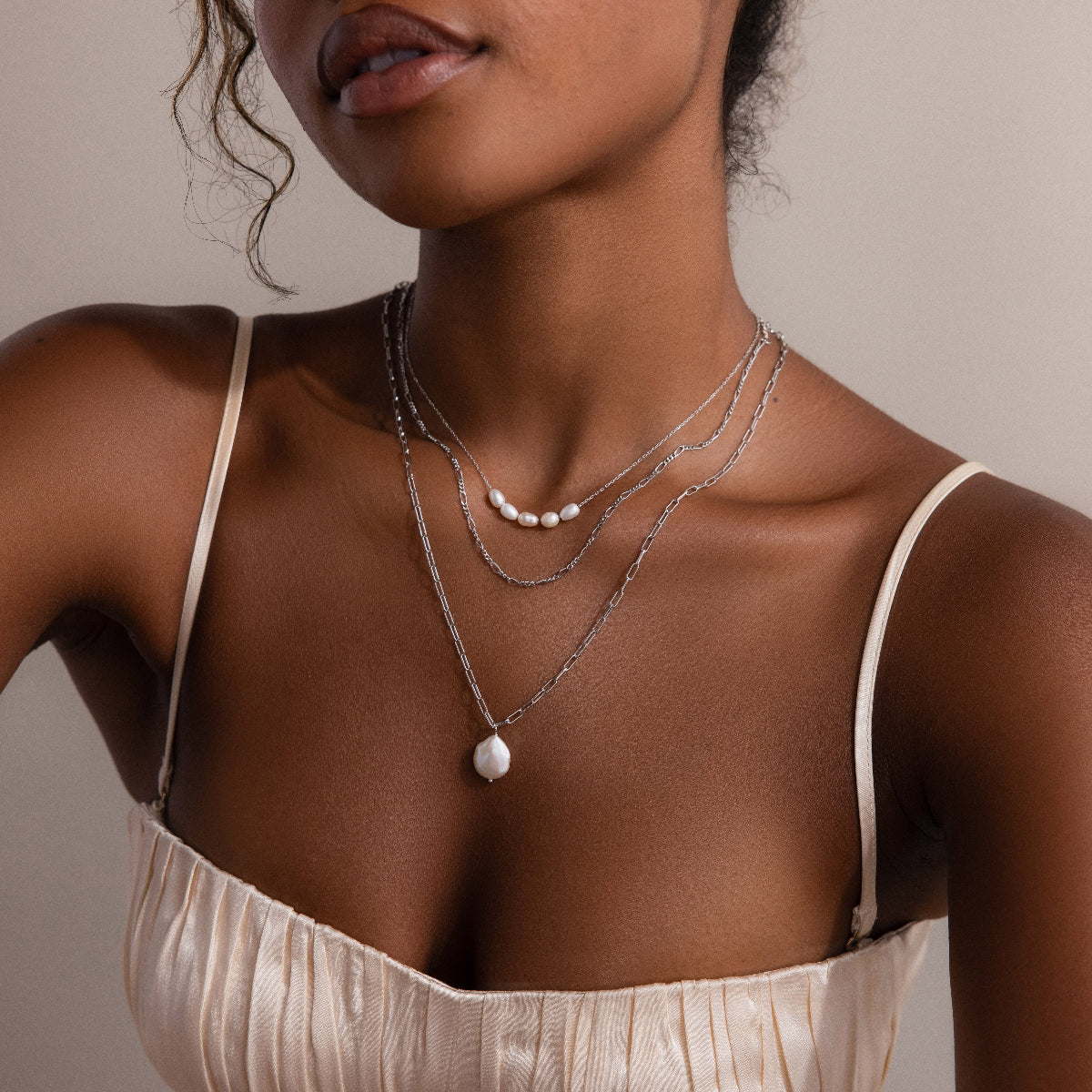 Close-up of a woman wearing layered silver necklaces with a neutral background