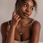 Woman wearing a silver link chain necklace with a pearl pendant against a neutral background