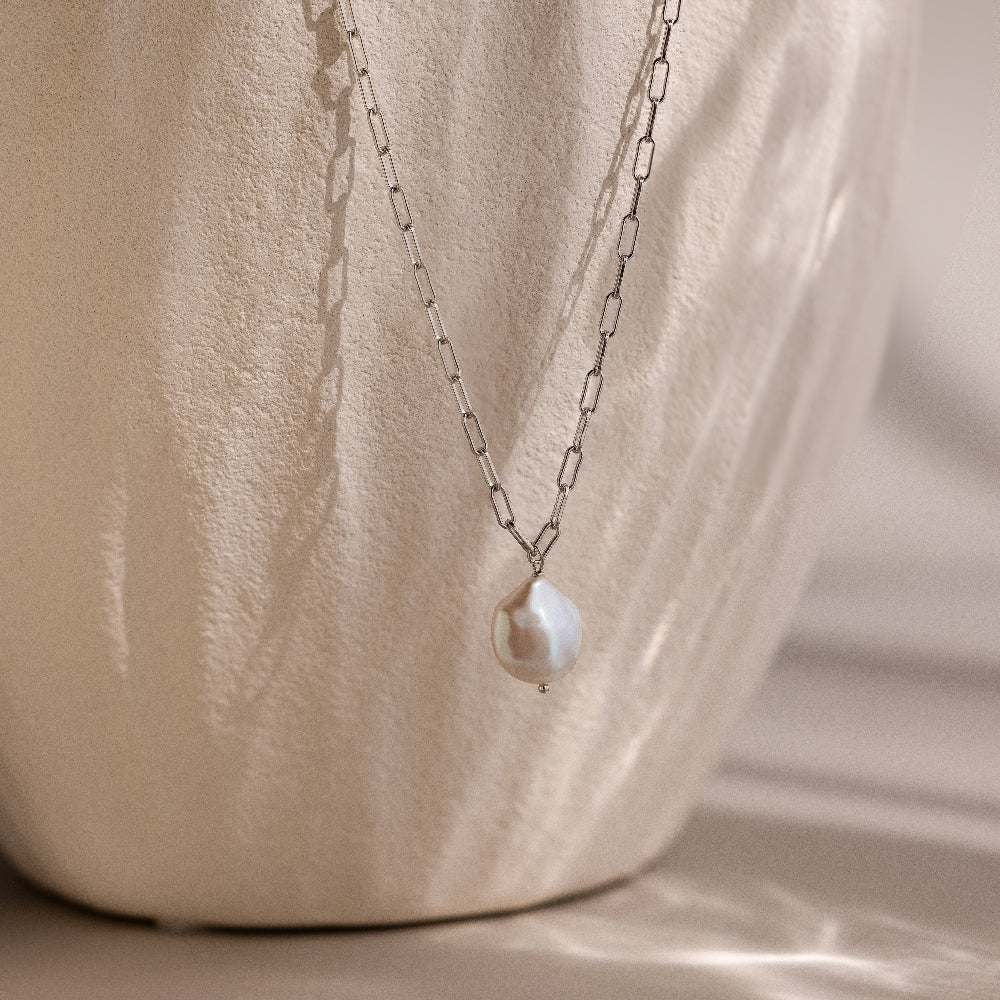 Silver link chain necklace with a pearl pendant on a beige stone background