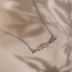 Dainty silver charm necklace with 'mama' pendant on a beige background