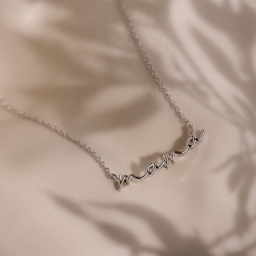 Dainty silver charm necklace with 'mama' pendant on a beige background
