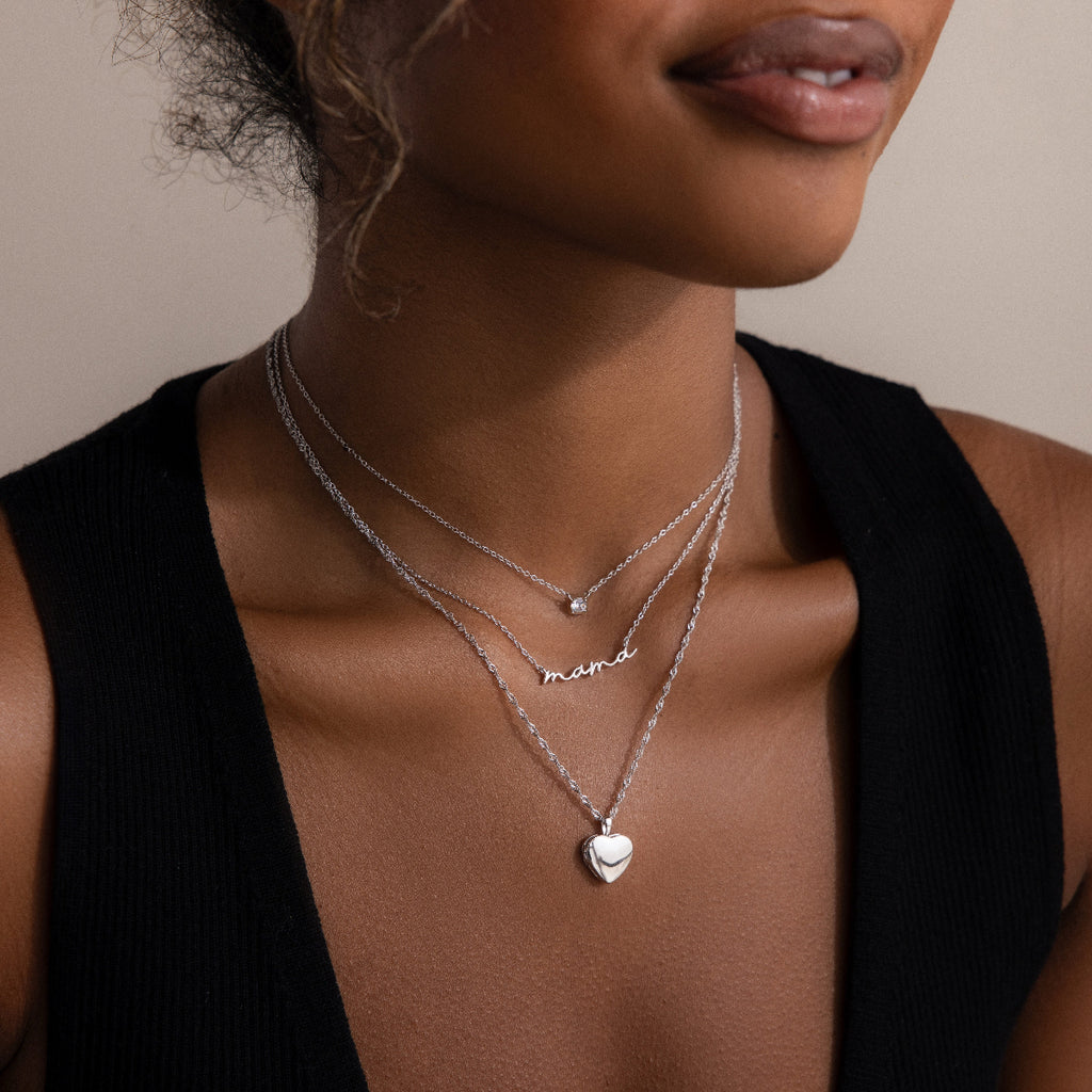 Woman wearing multiple silver necklaces and one with a heart pendant on a neutral background
