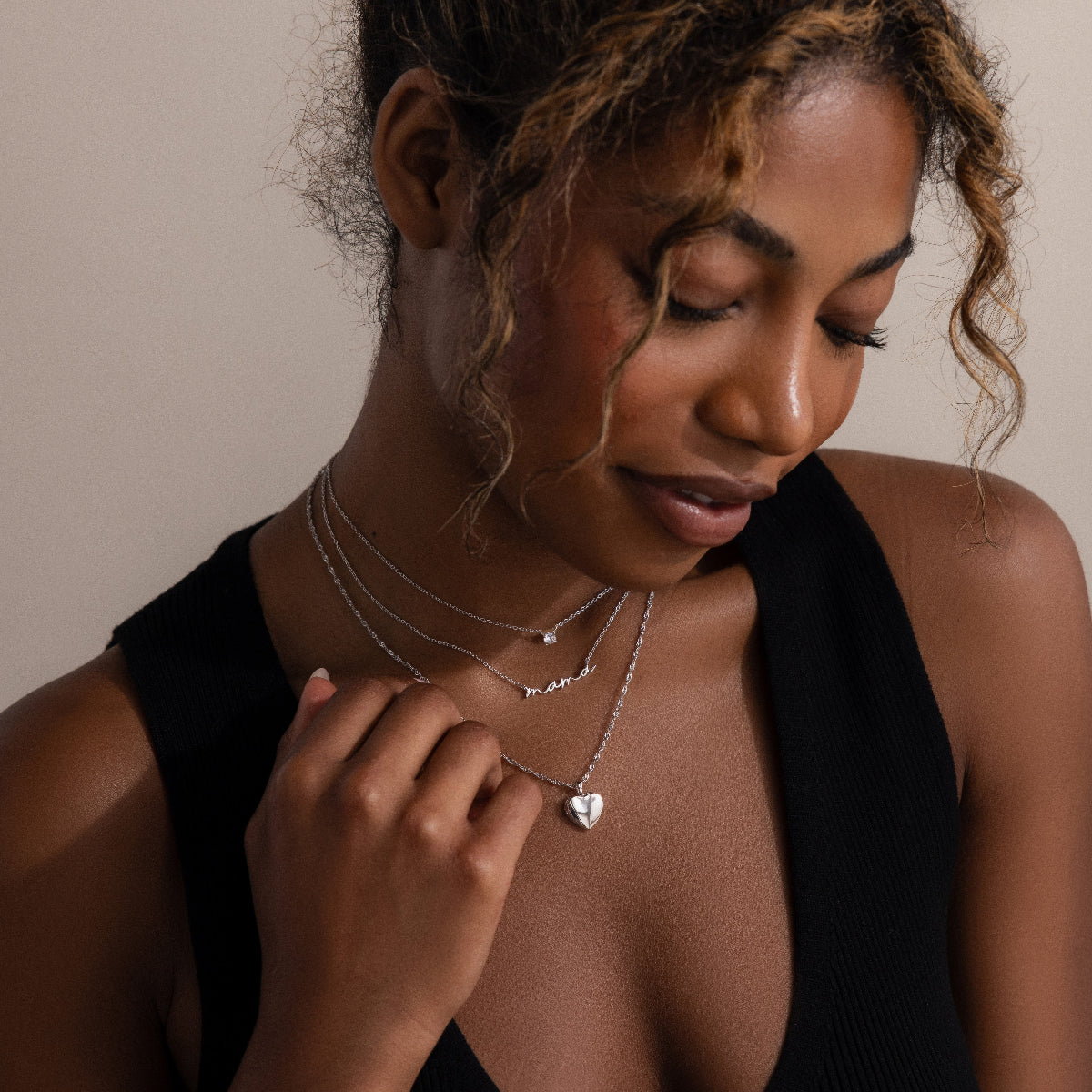 Woman wearing multiple silver necklaces with a neutral background