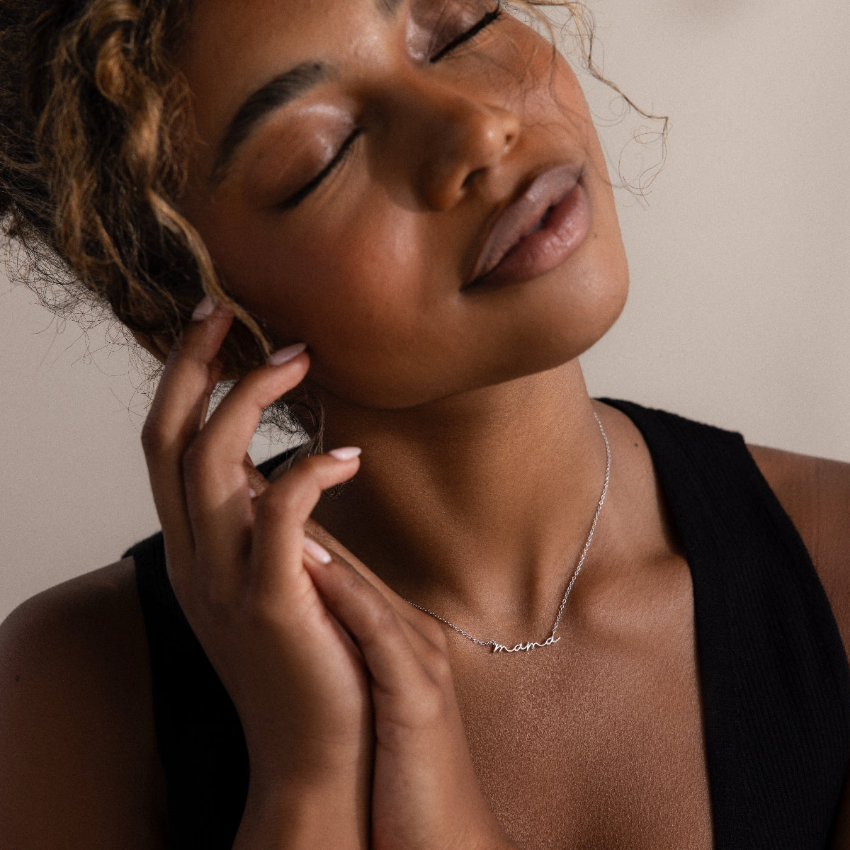 Woman wearing a silver mama charm necklace with a neutral background