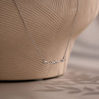 Silver necklace with 'mama' pendant on a textured beige background