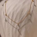 The Diamond Station Necklace in Silver and gold, adorned with small round gems, captures modern elegance as it rests on textured fabric.
