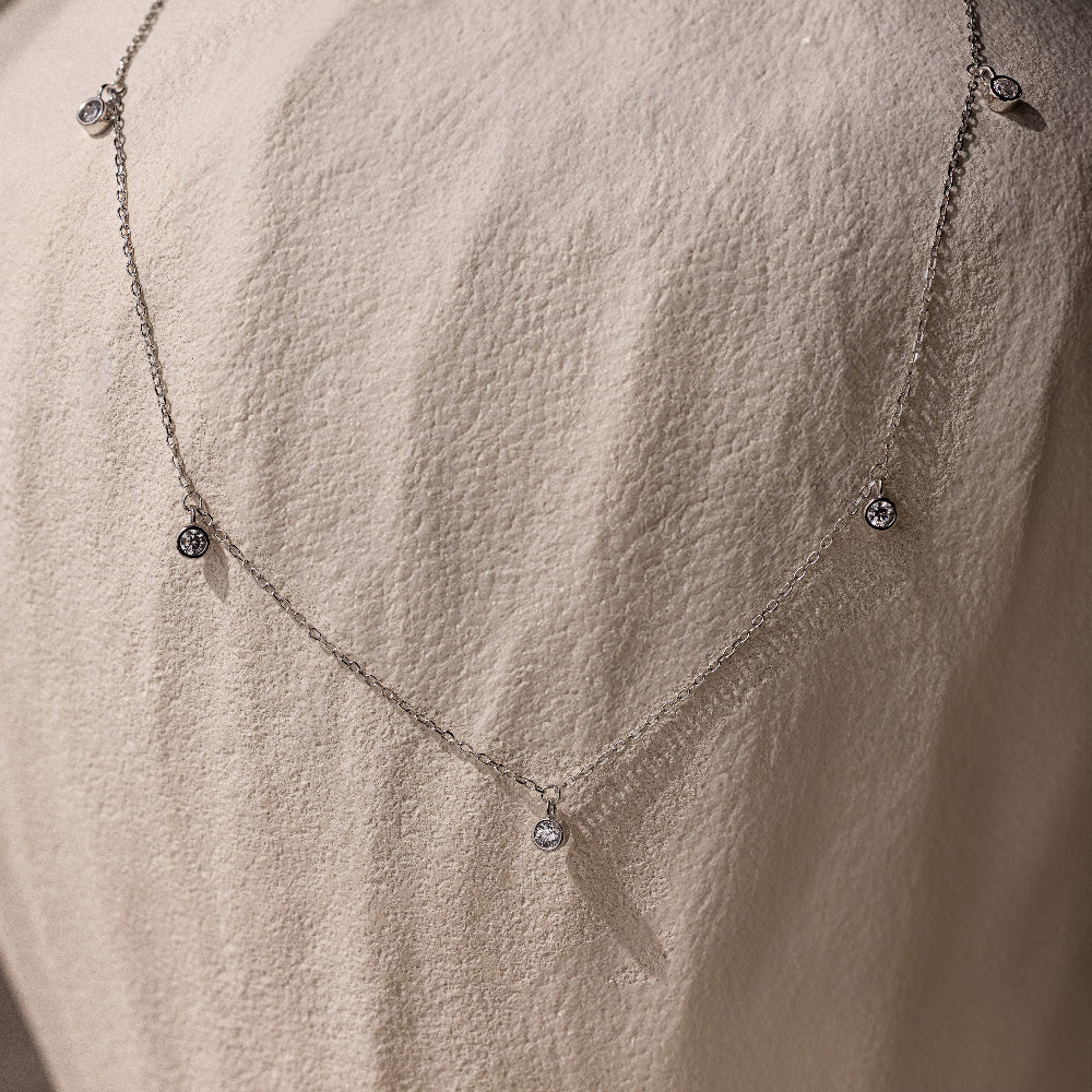 The Diamond Station Necklace in Silver, featuring delicate round pendants, is shown on a textured light fabric, highlighting its modern elegance.