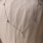 The Diamond Station Necklace, featuring delicate pendants, is shown on a textured stone—an elegant, timeless accessory that adds modern sophistication to any look.