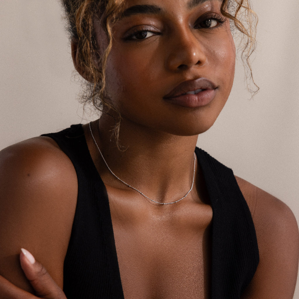 Woman with curly hair wearing a black sleeveless top and the Satellite Necklace in Silver—perfect for layering or adding an elegant touch when worn alone.