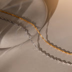 The Singapore Twist Necklace is displayed on a smooth stone surface in gold and silver with soft lighting and gentle shadows.