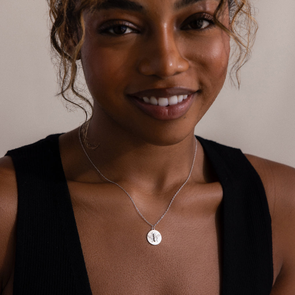 Smiling woman wearing a black top and the Bee Coin Necklace in Silver with a round pendant.