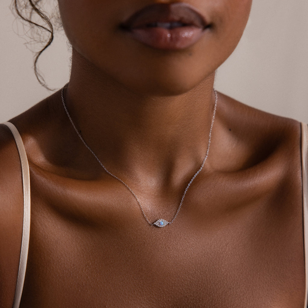 A woman wears the Opal Eye Necklace in Silver, featuring a delicate blue opal pendant, shown from shoulders to chin.