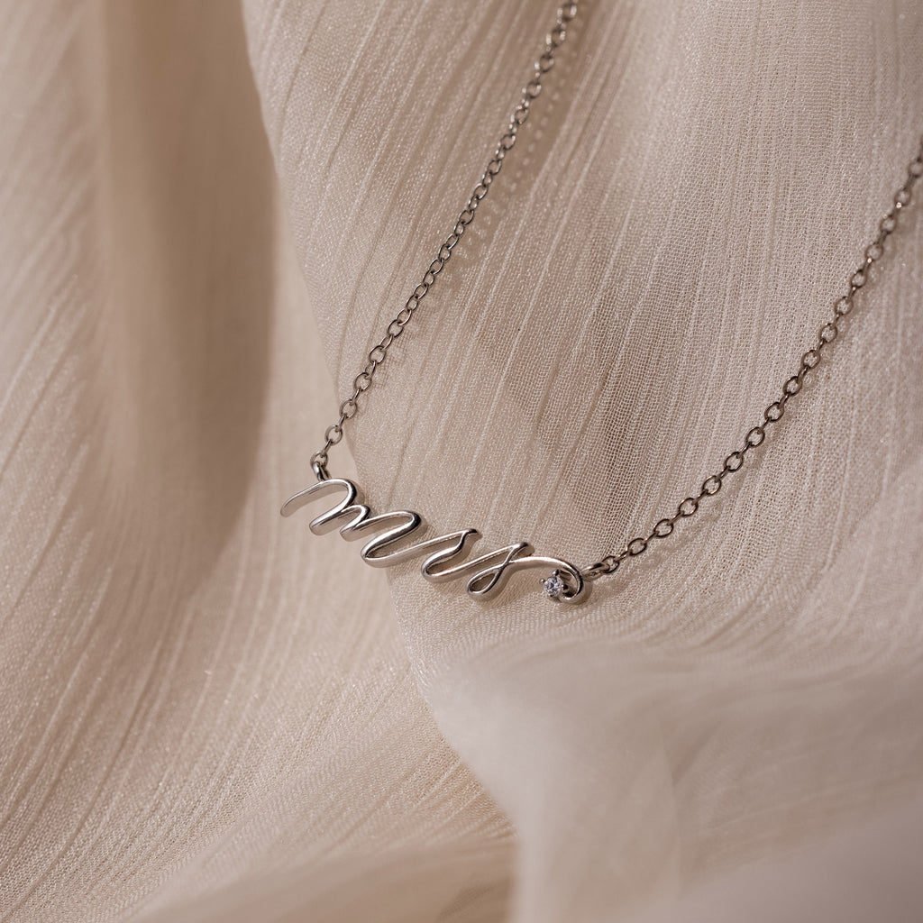 The Mrs. Necklace in Silver, shown on a soft beige fabric, makes an ideal wedding gift for any bride-to-be.
