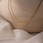 The Mrs. Necklace in silver and gold is displayed on a textured neutral background—an elegant and thoughtful wedding gift for any bride-to-be.