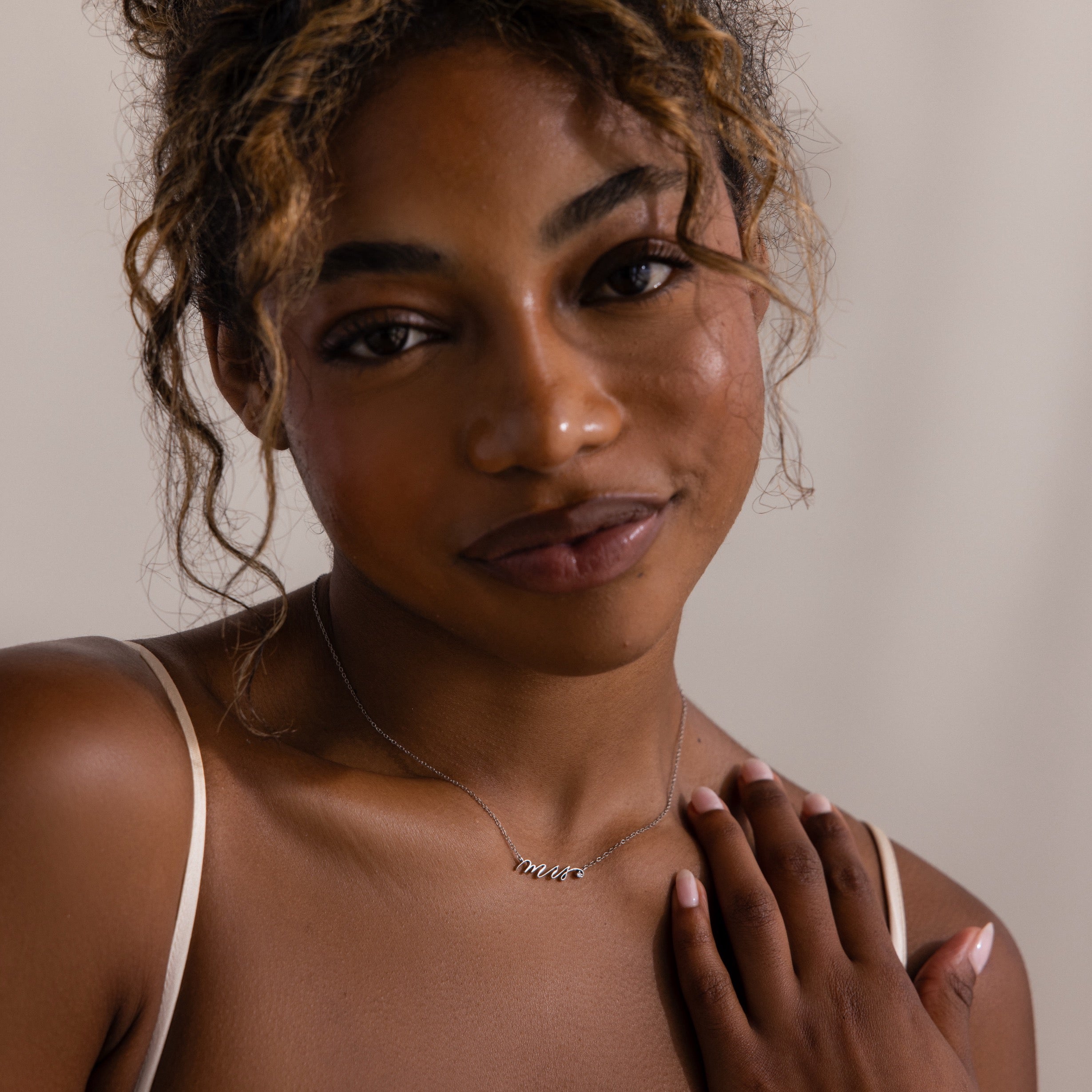 Woman with curly hair in a thin strap top wears the Mrs. Necklace in Silver, smiling softly—a perfect look for any bride-to-be.
