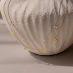 The Mama Letter Necklace in Silver and Gold, elegantly draped over a textured white vase, is a stylish tribute to motherhood and makes a thoughtful gift for any mom.