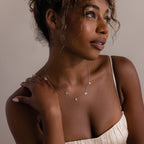 Woman in a cream dress wearing the Mama Letter Necklace in Silver, gazing thoughtfully to the side—a beautiful tribute to motherhood and an ideal gift for mom.