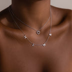 A woman wears two silver necklaces: a Mama Letter Necklace in Silver and one with a small heart pendant—a thoughtful gift to celebrate motherhood.